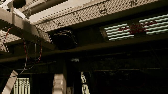 A detailed view shows wires and a ventilation system inside a building. The structure appears industrial with various elements visible. The setting is indoors with artificial lighting.