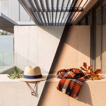 Autumn fashion accessories, straw hat and plaid scarf, placed on a concrete ledge with autumn leaves