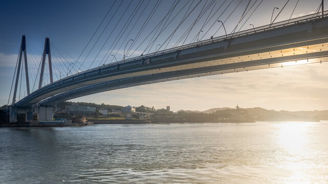 Low Angle View of Cable-Stayed Jindo Bridge with Golden Sun Glinting Over Ocean Waves