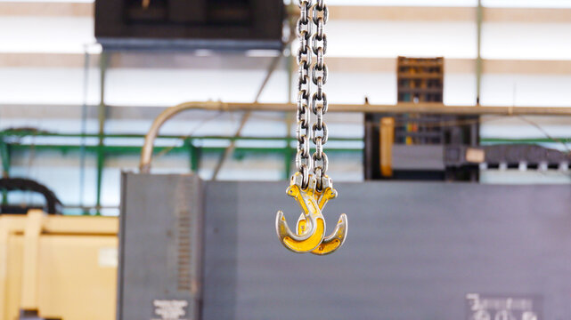 Lifting hooks and chains used in the production process. The hooks are suspended from chains above the work area and are used for lifting and moving heavy workpieces or materials.