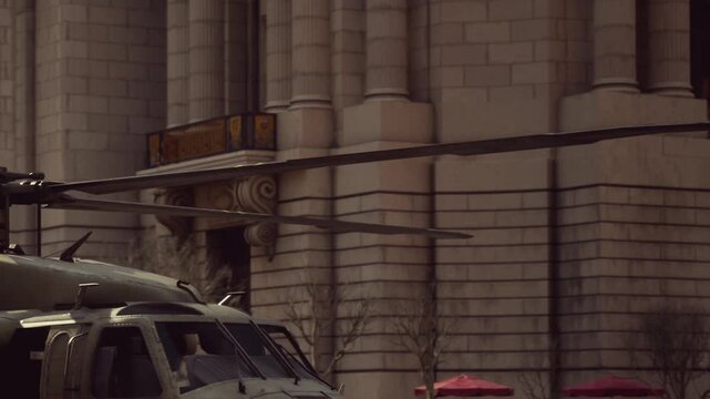 A helicopter is parked on the street in front of a large stone building. People walk nearby, and there are some umbrellas set up along the sidewalk.