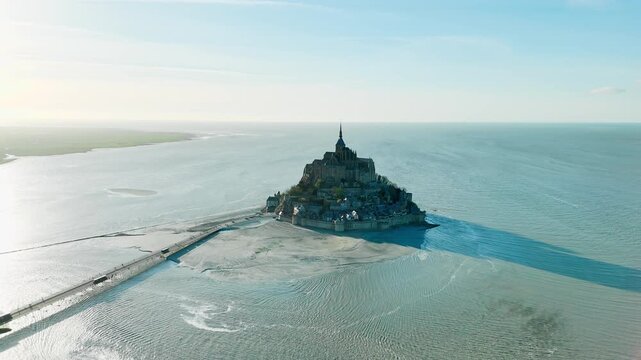 Mont Saint Michel rises above exposed sand flats in Normandy, France. Medieval island abbey on tidal bay for heritage and coastal landmark