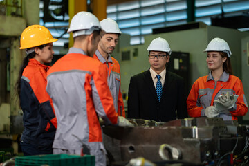 Fototapeta premium A diverse team of engineers and factory workers in safety helmets meet with a manager in a suit, discussing industrial machinery and manufacturing equipment inside a modern factory plant.