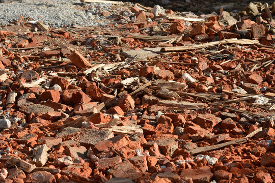 A detailed ground level view of construction demolition rubble consisting of broken red bricks, splintered wooden planks, and concrete pieces scattered on a construction site.