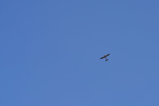 A small single engine propeller airplane cruising high overhead against a vast and completely clear bright blue sky.
