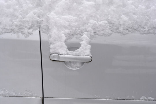 A close up shot of a silver car door handle partially covered in fresh white fluffy snow during a cold winter day.