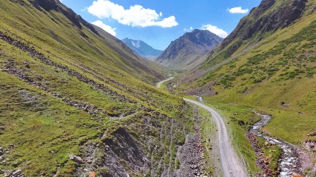 Mountain road in the mountains. Alpine landscape with a road in narrow valley to snow peaked mountains. Drone video of scenic mountain landscape.