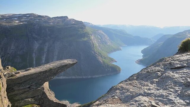 Dramatic summer view from Trolltunga above Ringedalsvatnet in Norway, with rugged cliffs, blue water, and distant mountains.