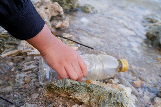 Hand picking up discarded plastic bottle on ocean shore for beach cleanup and environmental conservation