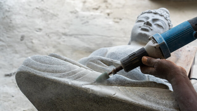 Sculptor using angle grinder to carve reclining Buddha statue from stone traditional craftsmanship