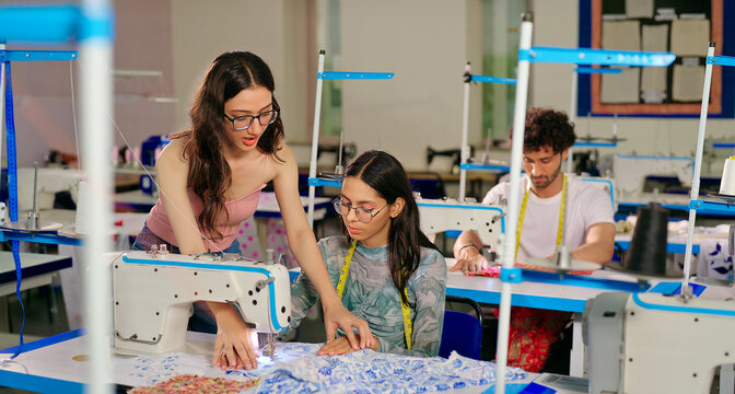 Indian young adult gen z woman lady wear tape around neck talk learn new clothes craft sewing course. Teen pupil girl female sitting desk help to stitch teach casual skill day indoor class room place