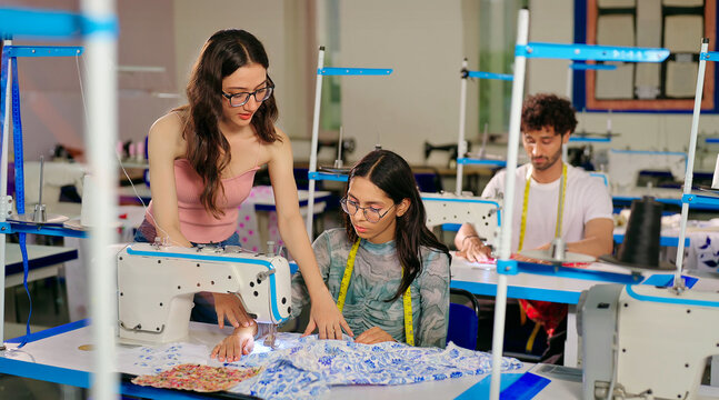 Indian young adult gen z woman lady wear tape around neck talk learn new clothes craft sewing course. Teen pupil girl female sitting desk help to stitch teach casual skill day indoor class room place