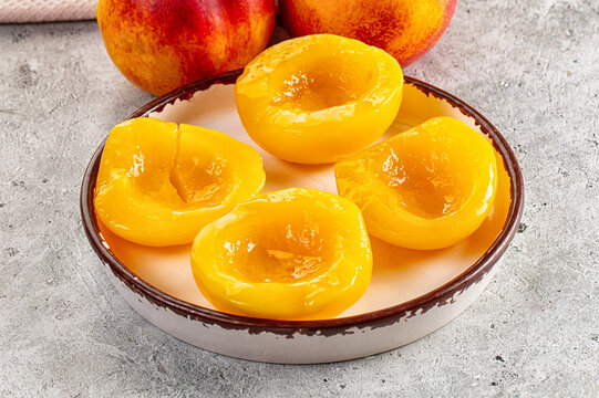 Fresh peach halves on ceramic plate with whole peaches in background