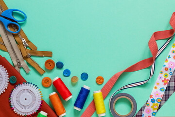 Assorted sewing and tailoring tools arranged on a pastel turquoise background, featuring thread...