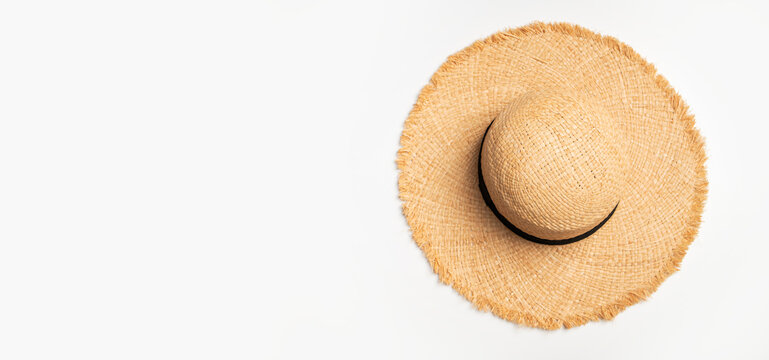 Straw sun hat on white background viewed from above, featuring wide frayed brim and black band. Summer headwear suits beach styling, vacation campaigns, travel content and seasonal fashion