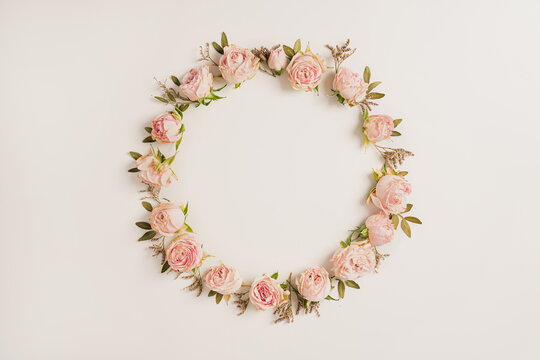 Pink rose circle wreath with leafy elements creating decorative round frame arrangement on light neutral background