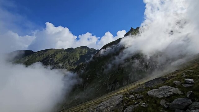 Dramatic clouds rolling over a steep mountain slope with a tiny hiker.