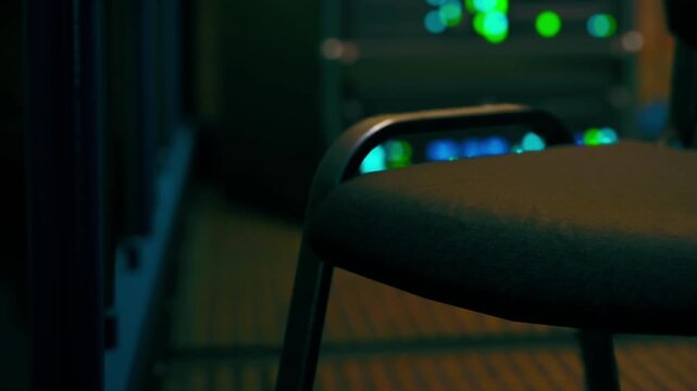 A chair is positioned in a room with low lighting. Various equipment is visible in the background, suggesting a work or technical environment. Nighttime adds to the atmosphere.