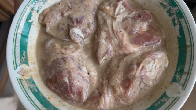 Raw chicken pieces marinating in creamy sauce on decorative plate, food preparation, cooking ingredients, marinated meat, homemade dinner