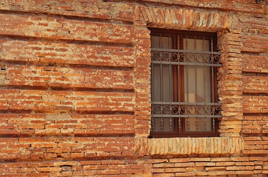 An old brick wall with an antique window and wrought iron grille.
A close-up of the texture of an old red brick wall with a wooden window frame and decorative metal grilles.