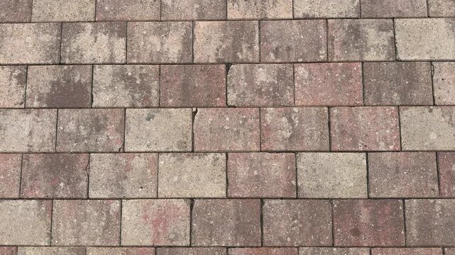 Weathered paving stones in staggered brick pattern, textured pavement background with brown gray red tones, outdoor walkway surface