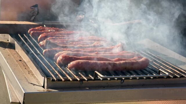 Close-Up of Hands Grilling and Turning Sizzling Sausages on Barbecue Outdoors. A delicious close-up shot of hands turning sizzling sausages over a hot grill grate at an outdoor picnic.