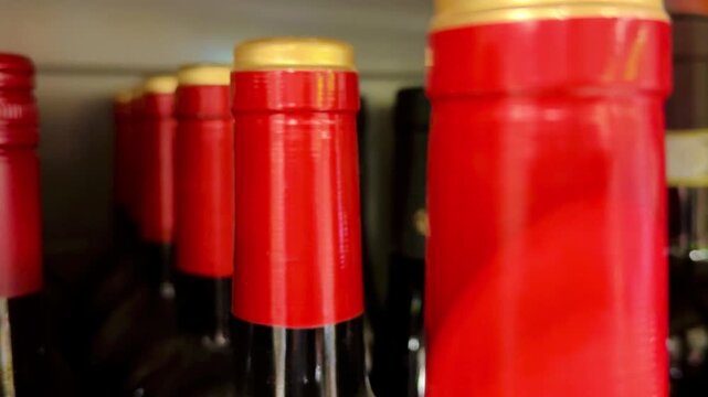 Close-up red wine bottle necks, rows of assorted brands on store shelf with glossy foil caps and visible cork tops, tight framing