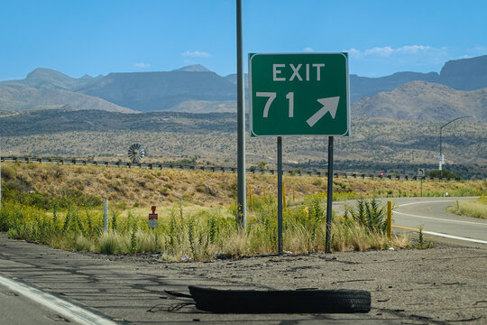 Highway exit sign indicating Exit 71 with an arid mountain landscape background in Arizona.