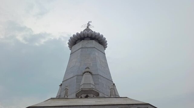 Low angle shot of white marble Hindu temple spire with saffron flag against cloudy sky