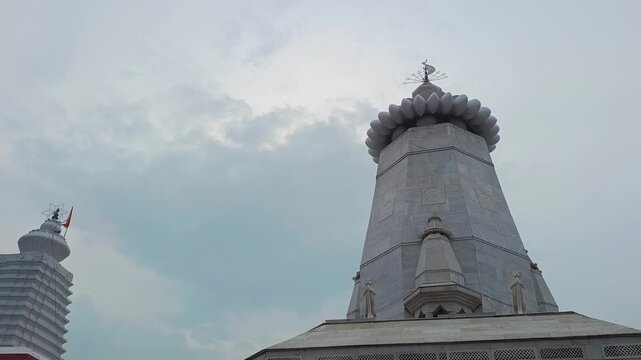 Low angle shot of white marble Hindu temple spire with saffron flag against cloudy sky