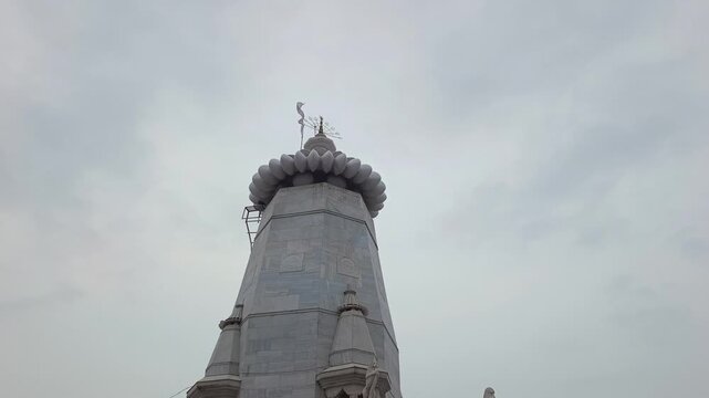 Low angle shot of white marble Hindu temple spire with saffron flag against cloudy sky