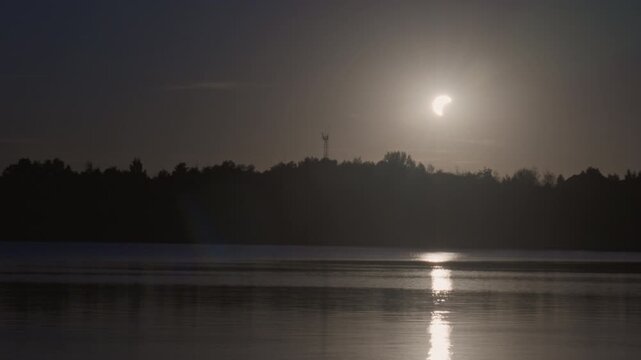 Partial solar eclipse over calm lake with reflection
