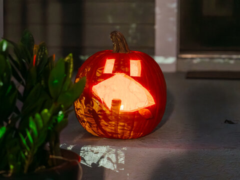 A glowing carved pumpkin lights up a front porch at night. The classic jack o' lantern is a timeless symbol of Halloween celebrations.