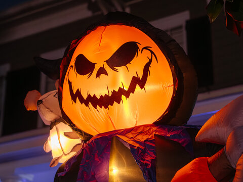A glowing inflatable pumpkin character lights up a front yard during Halloween night. The sinister face creates a dramatic and spooky holiday display.