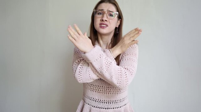 Woman crosses her arms in a no and stop gesture asking someone not to do it while showing clear refusal prohibition and a serious pleading expression toward camera firmly