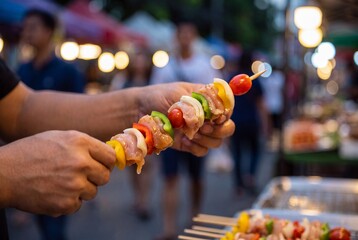 Obraz premium Street Food Vendor Assembles Meat and Vegetable Skewers at Night Market