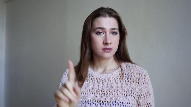 Young woman raises one index finger with closed eyes making a clear no gesture expressing refusal disagreement warning disapproval rejection and firm personal boundaries