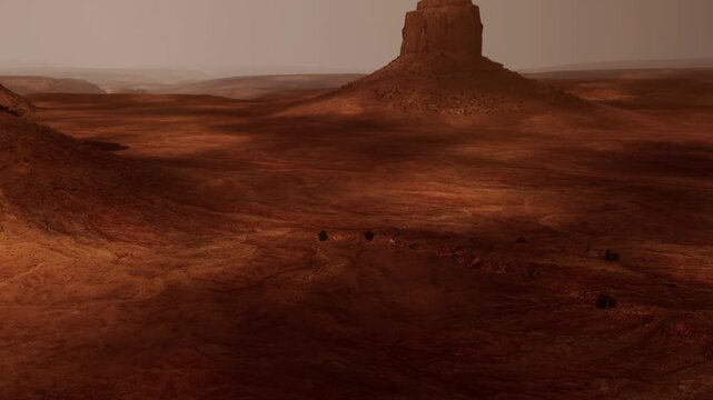 A view of Monument Valley showing stone structures and sandy ground. The scene captures the dry, rugged terrain under a hazy sky. Shadows create patterns on the surface.