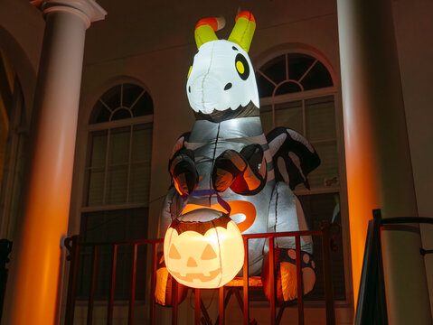 A large skeleton zebra inflatable holds a bright jack-o-lantern on a residential porch. Warm orange lighting creates a festive and spooky Halloween display at night.