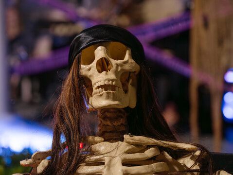 A human skeleton decoration with long dark hair appears in a close-up Halloween display. The detailed skull, teeth, and bones create a creepy horror atmosphere at night.
