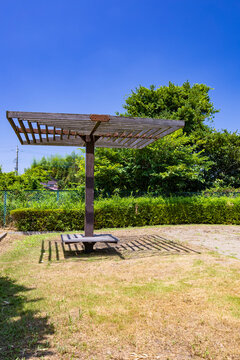 青空の広がる日本の公園に設置された木製のパーゴラと日よけ棚のある休憩スペース（縦構図）