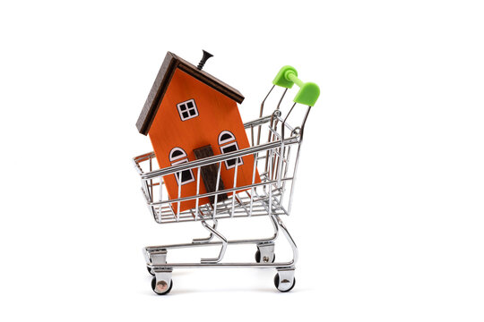 A symbolic wooden house in a miniature shopping cart against a white background.