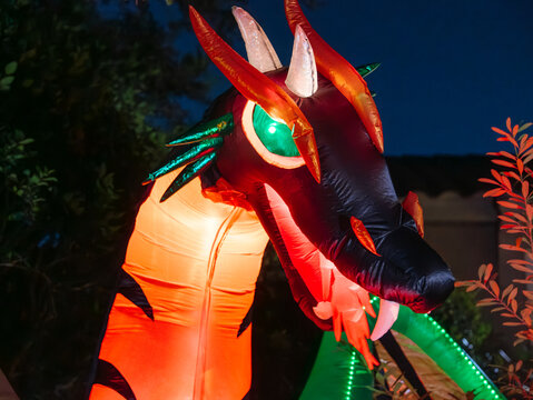 A glowing dragon inflatable features red horns, white fangs, and a bright green eye. The colorful monster creates a dramatic outdoor Halloween decoration at night.