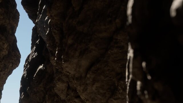 The scene shows a narrow gap between two large rocks under bright sunlight. The rocks are rough and uneven, creating a natural passageway.