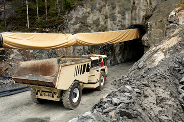 Heavy construction machinery, a dump truck, positioned near a tunnel entrance, surrounded by rocky terrain and a protective tarp covering the tunnel opening © Kateryna Muzhevska