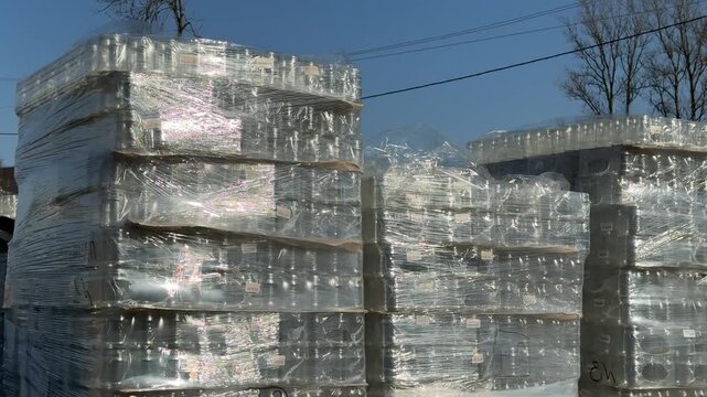 Stacks of glass bottles on pallets, outdoor hardware store sidewalk, clear liter jars wrapped in shrink film, sunlight sparkling