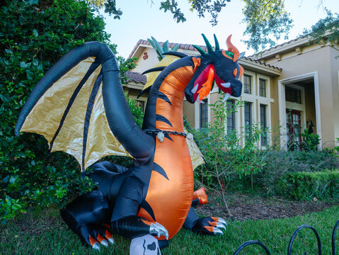 A massive inflatable dragon decorates the front yard of a suburban home for Halloween. The colorful display creates a fun and eye-catching seasonal neighborhood attraction.