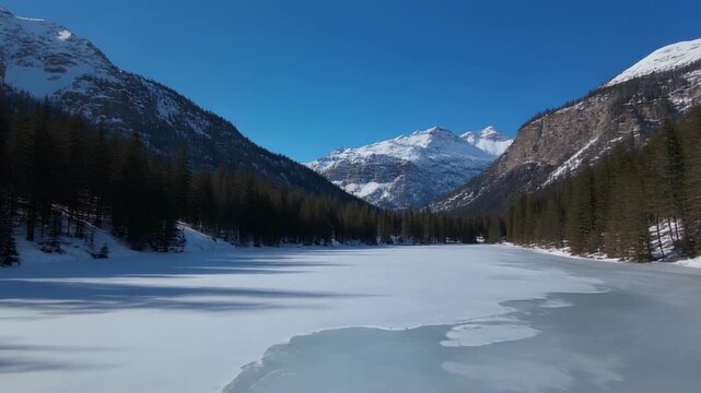 Snowy Mountain Lake Landscape with Rippling Ice Under Clear Blue Sky Cinematic Aerial