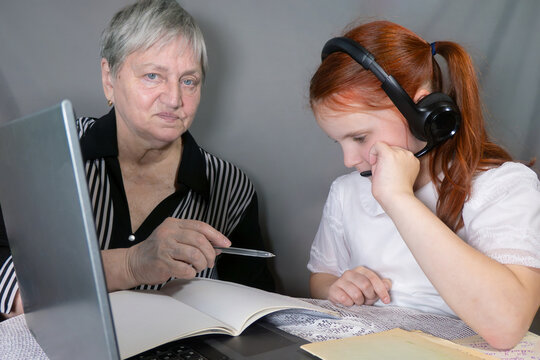 grandma helps granddaughter to school pupil wearing headphones studying online from home making notes. distance learning on laptop. A parent comforts a child during an online learning session. lesson