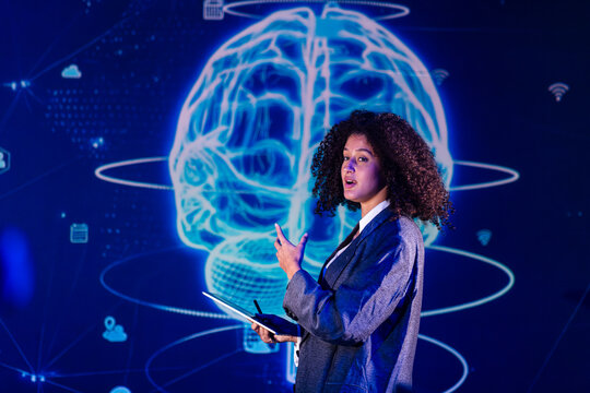 Woman speaking in front of a large digital brain display while holding a tablet